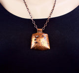 textured copper pendant with black seed beads on copper chain